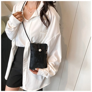 Detail of minimalist black leather crossbody phone bag featuring a white pearl button closure