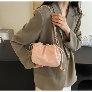 Dettaglio della borsa a secchiello rosa con texture arricciata e tracolla a catena dorata