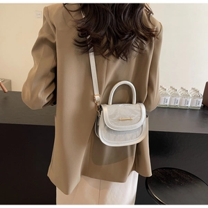 Detailed view of silver metallic mini saddle bag worn with a tailored brown blazer
