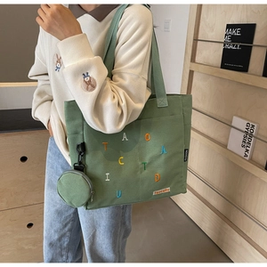 Close-up of forest green canvas tote bag with colorful embroidery and a round coin purse