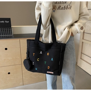 Detail of black canvas tote bag with colorful letter embroidery and small coin purse attachment