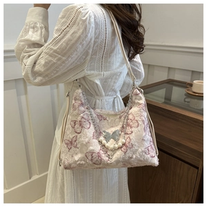 Detail of butterfly print tote bag with pearl chain and silver charm on cream faux leather