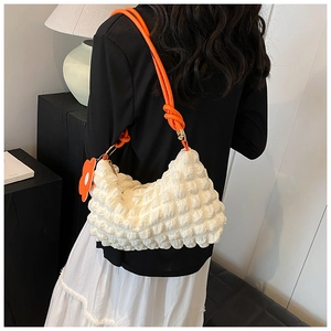 Detailed shot of white bubble textured shoulder bag with orange tube strap and flower charm