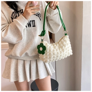 Detail of white bubble textured shoulder bag with green rope handle and floral charm