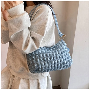 Detail of light blue pleated puffy bag with golden metal rings on soft shoulder strap