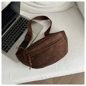 Détail du sac selle en velours côtelé marron avec imprimé fraise sur canapé blanc