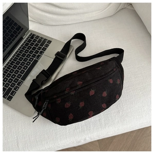 Détail du sac selle en velours noir à motif fraise sur canapé blanc à côté d'un laptop