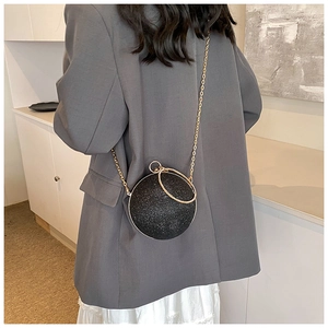 Detail view of a spherical black sequin bag with gold chain strap on a blazer