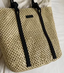 Detalle del bolso tote de paja beige con tejido calado y asas negras con cintas decorativas