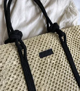 Detalle del bolso de paja tejido con asas de cuerda negra anudada y parche de cuero