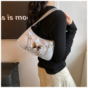 Bolso de hombro plateado metalizado con mariposa y cadena llevado por modelo