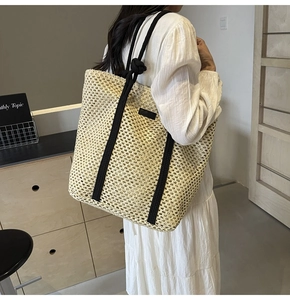 Detalle del bolso tote de paja beige con asas de cuerda negra gruesa llevado por una modelo