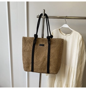 Detalle de un bolso tote de paja trenzada con diseño calado y correas de cuerda negra