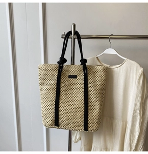 Detalle de bolso tote de paja calada beige con asas de cuerda negra en una percha