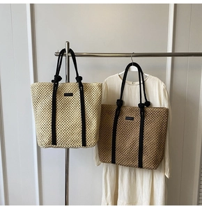 Detalle de bolsos tote de paja trenzada con asas de cuerda negra en un soporte