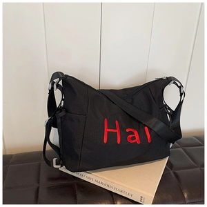 Versatile black nylon bag with red embroidery on a leather bench in lifestyle setting