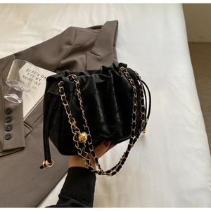 Detail of black pleated bucket bag with gold chain strap and spherical charm ornament