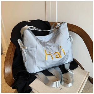 Detail of grey tote bag with gold Hai embroidery and adjustable strap on a chair
