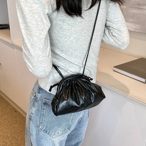 Fashionable black pleated drawstring crossbody bag with glossy finish on model