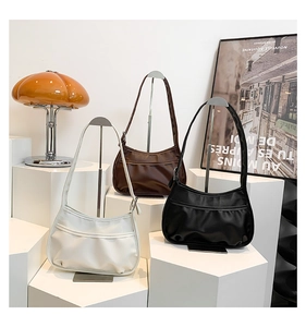 Three crescent shoulder bags in white, coffee and black on display stands