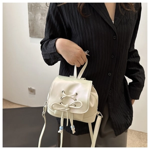 Detail eines Mini-Rucksacks in Creme mit Schleife, Kreuzschnürung und blauen Perlenakzenten