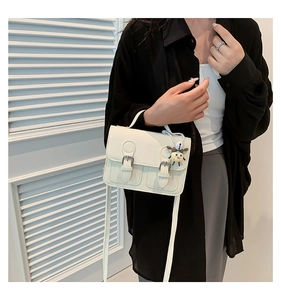 Detail of cream Cambridge satchel with metal buckles and a cute plush charm on strap
