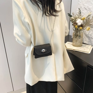 Mini black leather crossbody bag with silver planet buckle and chain strap on white blazer