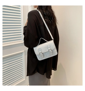 Light gray satchel bag with flap cover and twin buckles shown on shoulder strap