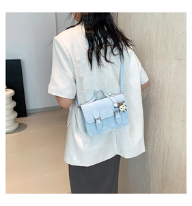 Detailed back view of a light blue messenger bag with a plush charm on a model
