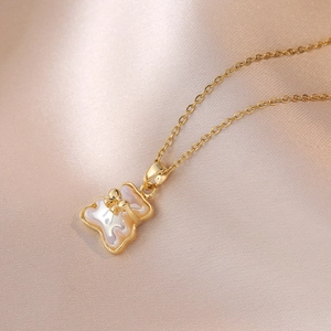 Detailopname van een gouden teddybeerketting met wit schelpinlay op zijden ondergrond