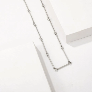 Collier minimaliste en métal argenté avec tiges et anneaux sur décor géométrique blanc