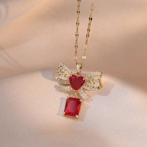 Golden bow necklace featuring a heart-shaped red crystal and pavé zircon accents
