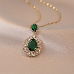 Collier pendentif émeraude en goutte d'or avec halo de zircons sur tissu en soie beige