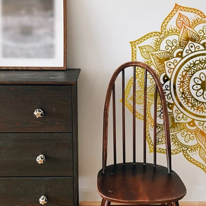 Detail of bohemian mandala wall sticker in gold gradient on a white wall with vintage furniture