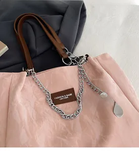 Détail d'un cabas rose en cuir texturé avec étiquette brune et bandoulière en chaîne