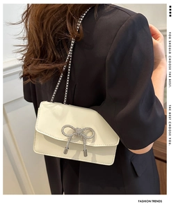 Detail of a creamy white PU leather crossbody bag with a silver rhinestone bow decoration