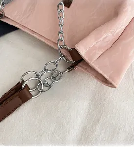 Détail du sac brillant rose avec chaîne argentée et connecteur en cuir marron
