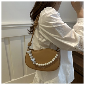 Detail of a brown leather saddle bag featuring a decorative heart and pearl chain strap