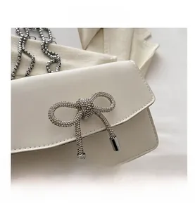 Close-up of sparkling rhinestone bow clasp and silver chain on creamy white bag