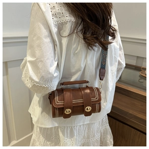 Brown cylinder crossbody bag with white stitching and vintage ethnic pattern strap