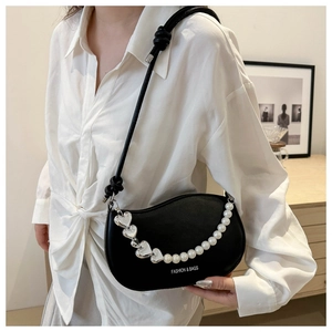 Detail of black crescent shoulder bag with pearl chain and silver heart charm on model