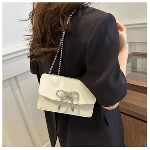 Détail d'un sac bandoulière en similicuir blanc crème avec nœud en strass et chaîne en métal