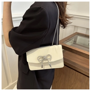 Vue latérale du sac bandoulière crème avec nœud en strass et chaîne sur modèle