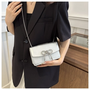Sac bandoulière argenté métallisé avec nœud en strass porté sur un blazer noir