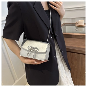 Petit sac carré argenté avec nœud en strass porté par un mannequin en veste noire