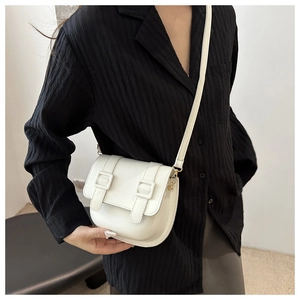 Close-up of white minimalist saddle bag with gold buckles and adjustable strap on a model