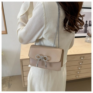 Détail du sac bandoulière en cuir PU beige avec nœud en strass argentés et bandoulière chaîne