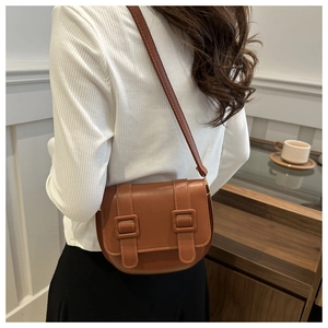 Detail view of a brown faux leather saddle bag with buckle straps worn by a model