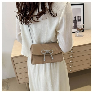 Détail d'un petit sac carré beige à chaîne orné d'un nœud en strass argentés étincelants