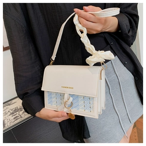 Detail of luxury plaid silk scarf handle and golden charm on cream leather bag